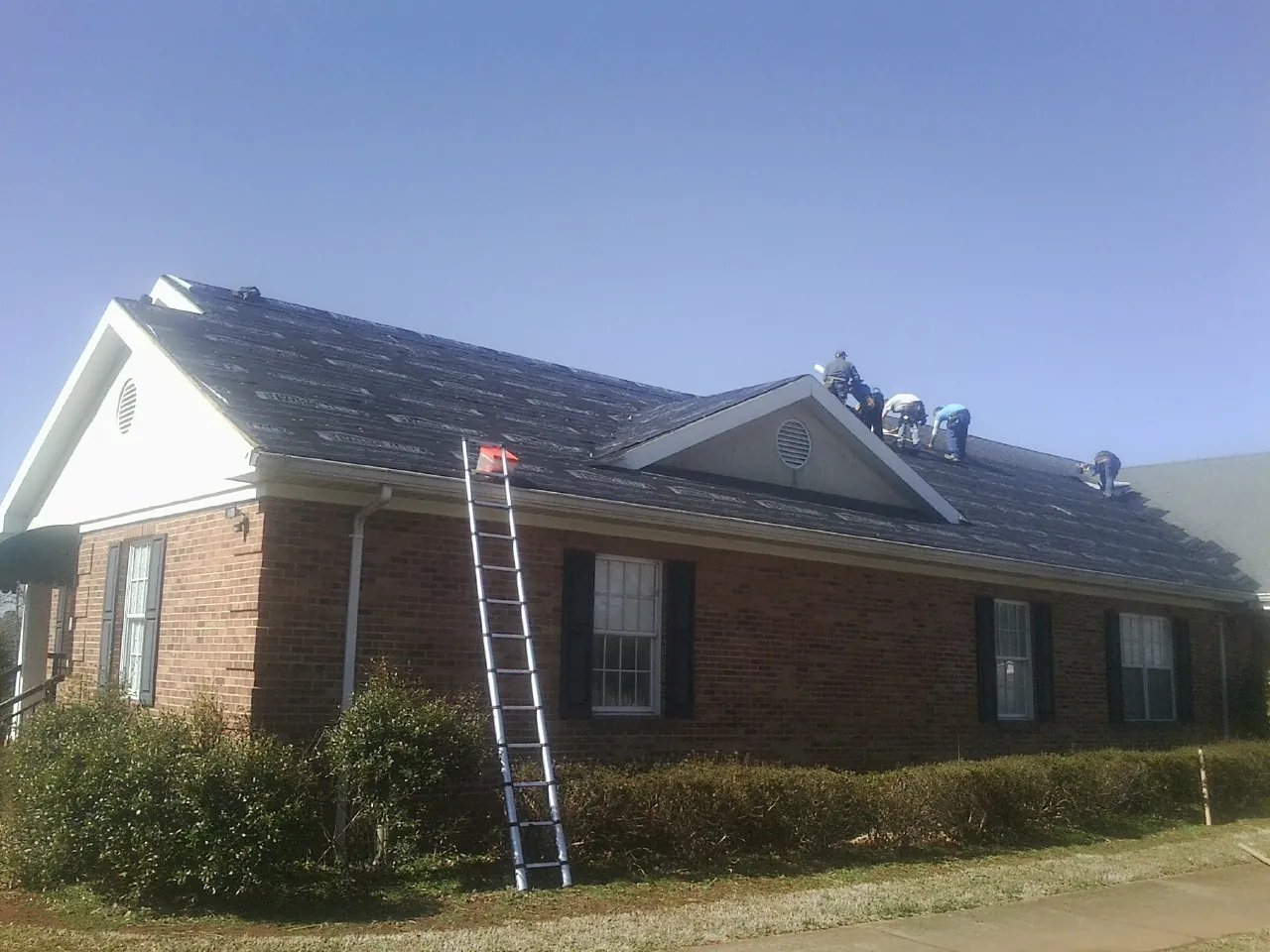 Crew tearing shingles off a brick ranch roof with a ladder set — Emergency Roof Repair work by our crew in Killingworth
