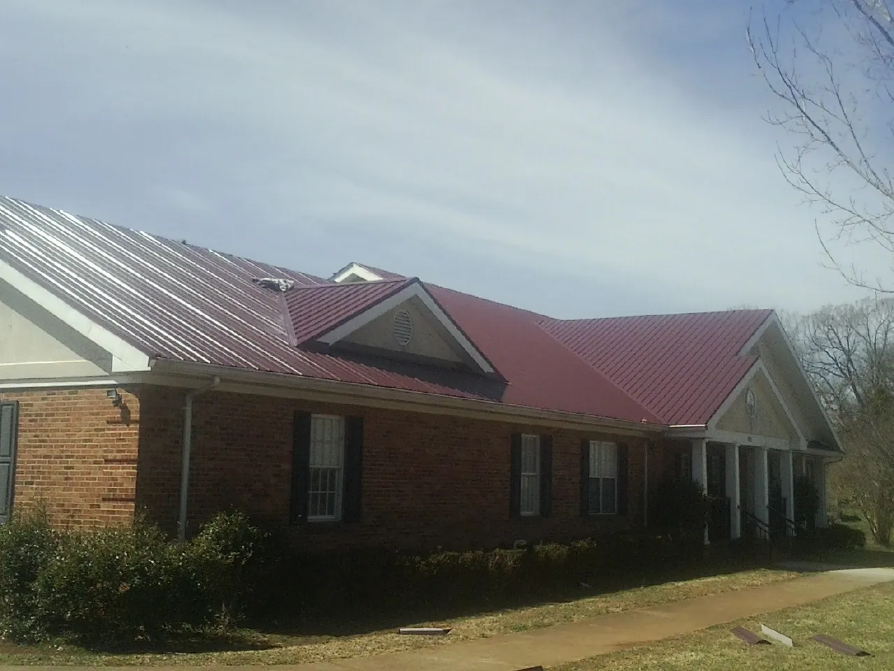 Red metal roof with gabled entries on a long brick building, from a Hail Damage Roof Repair job in Killingworth