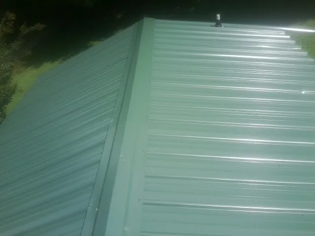 New green metal panels meeting at the ridge of a roof — Flat Roof Repair work by our crew in Killingworth