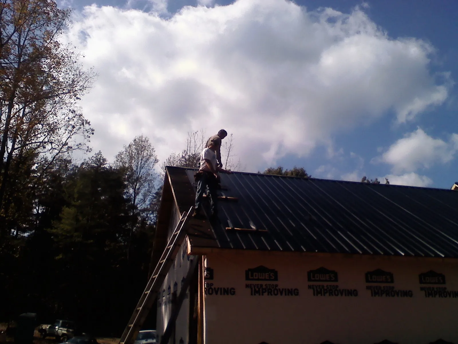 Roofer fastening dark metal panels high against a cloudy sky, from a Roof Inspection job in Killingworth