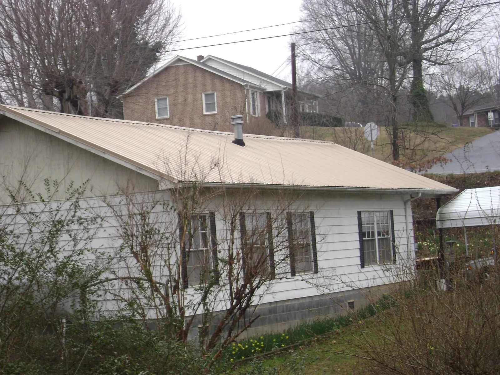 Tan metal roof on a white sided house set into a hillside — Commercial Roofing by Roofing Brothers in Killingworth